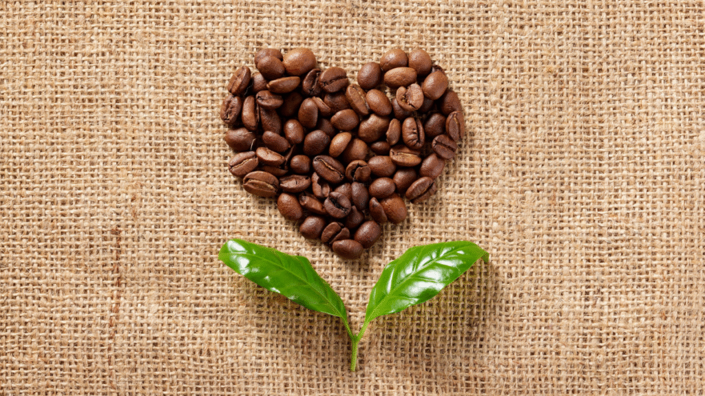 Geröstete Kaffeebohnen in Herzform auf Jutegewebe mit Kaffeeblättern